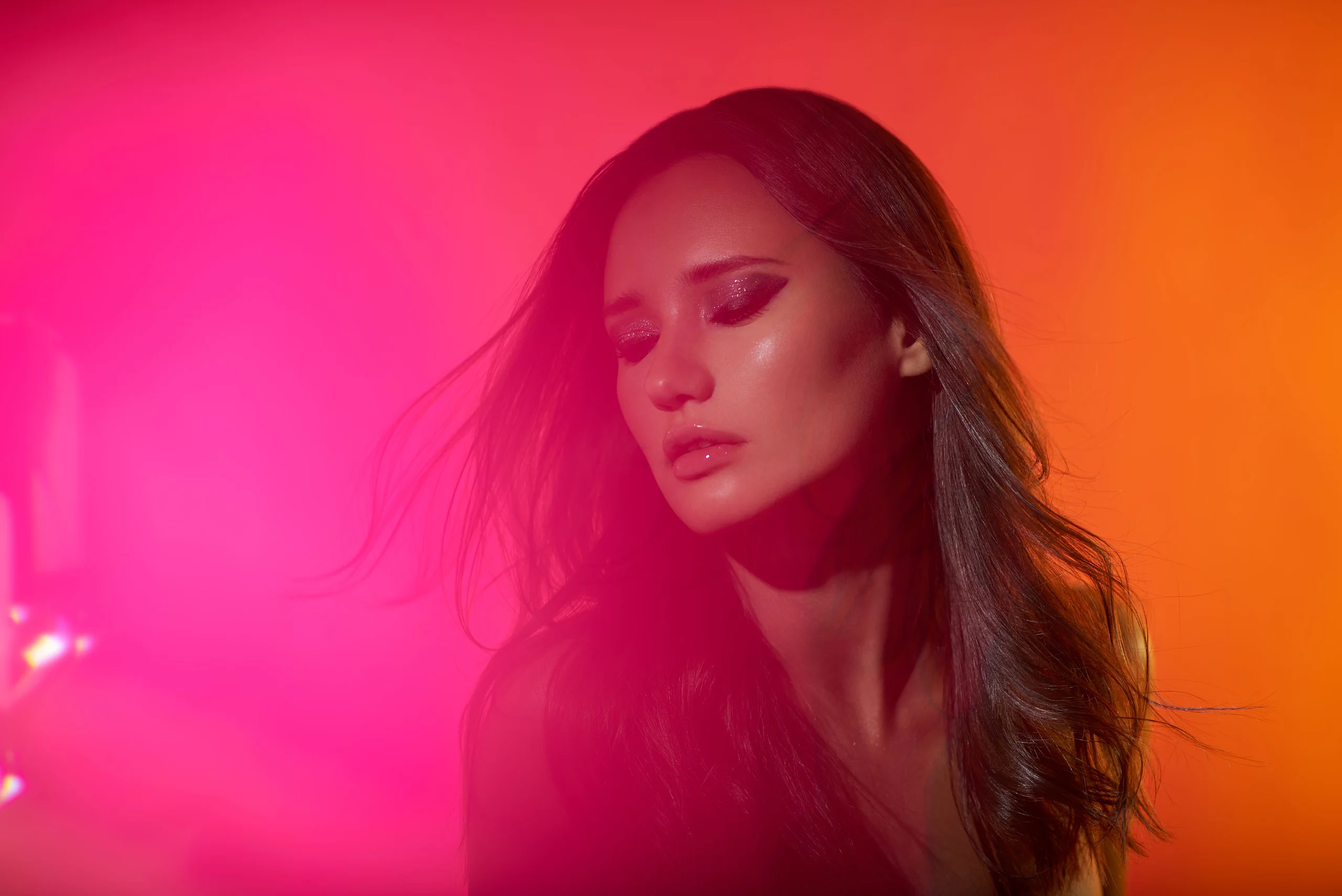 A beauty portrait with closed eyes, windswept hair, and vivid pink and orange light.