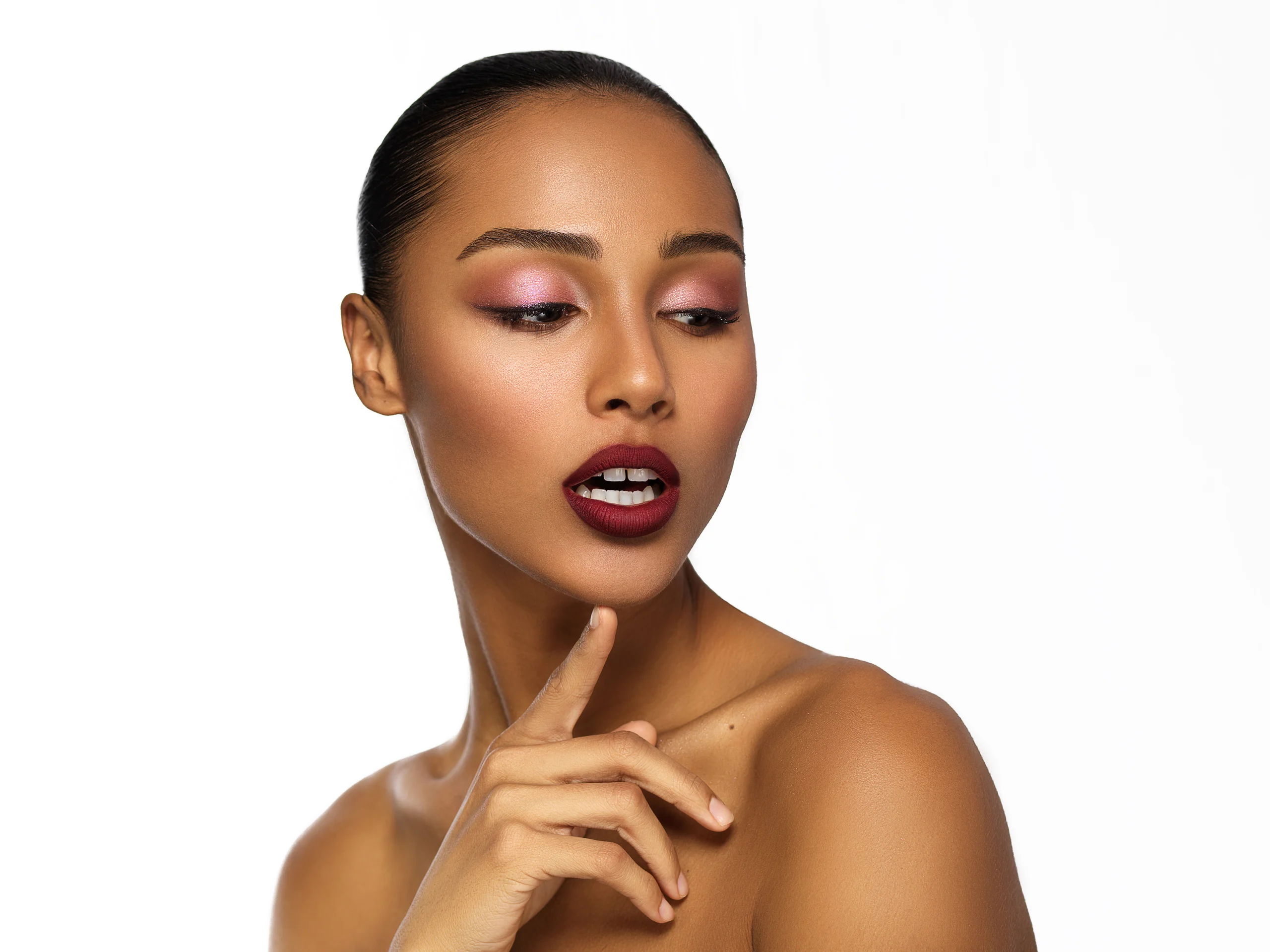 A beauty portrait with pink eye makeup and a hand beneath the chin against white.