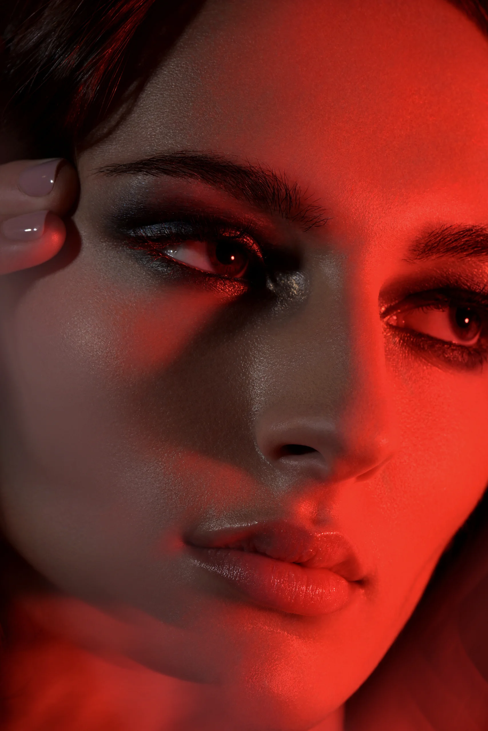 A close beauty portrait with dark eye makeup and red light across the face.