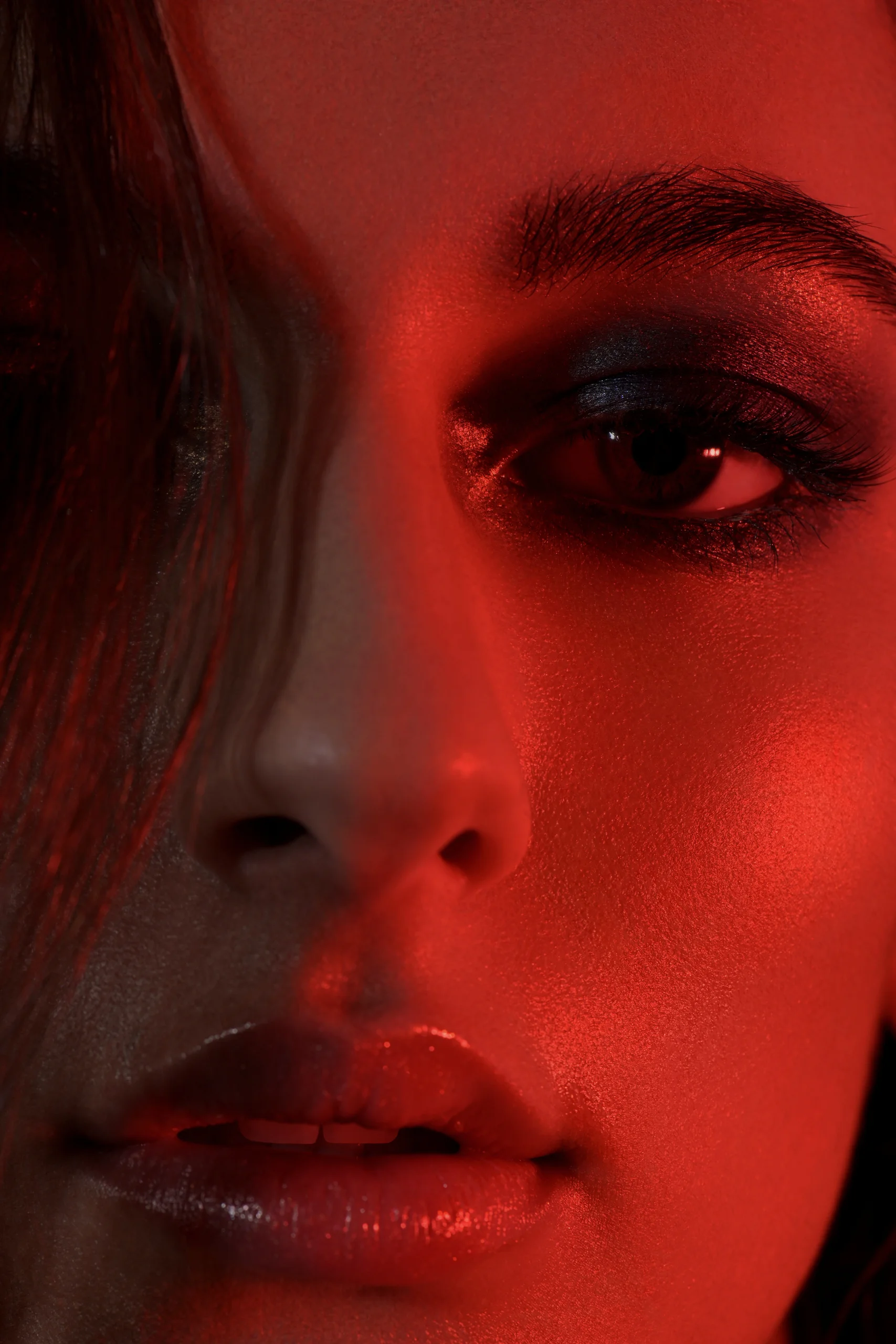 A close-up of eyes and glossy lips in deep red light.