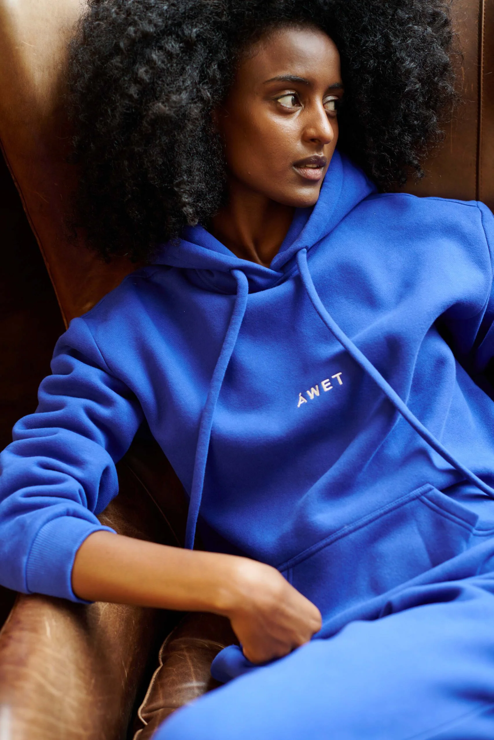A seated model in a vivid blue ÁWET hoodie.