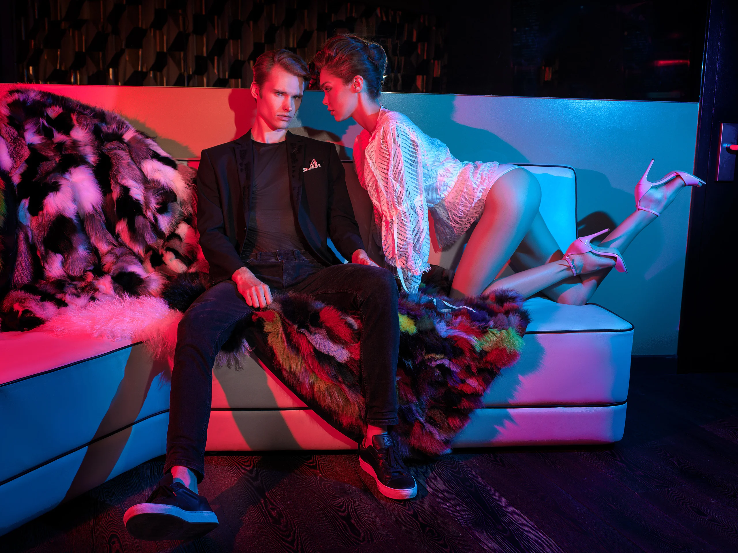 Two models posed together on a sofa under red and blue light.